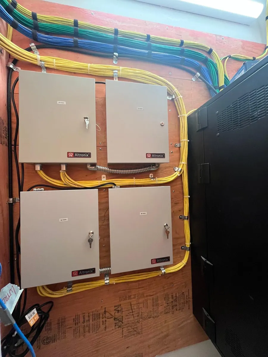 Four access control power supply enclosures mounted on a plywood backboard with neatly dressed cable runs