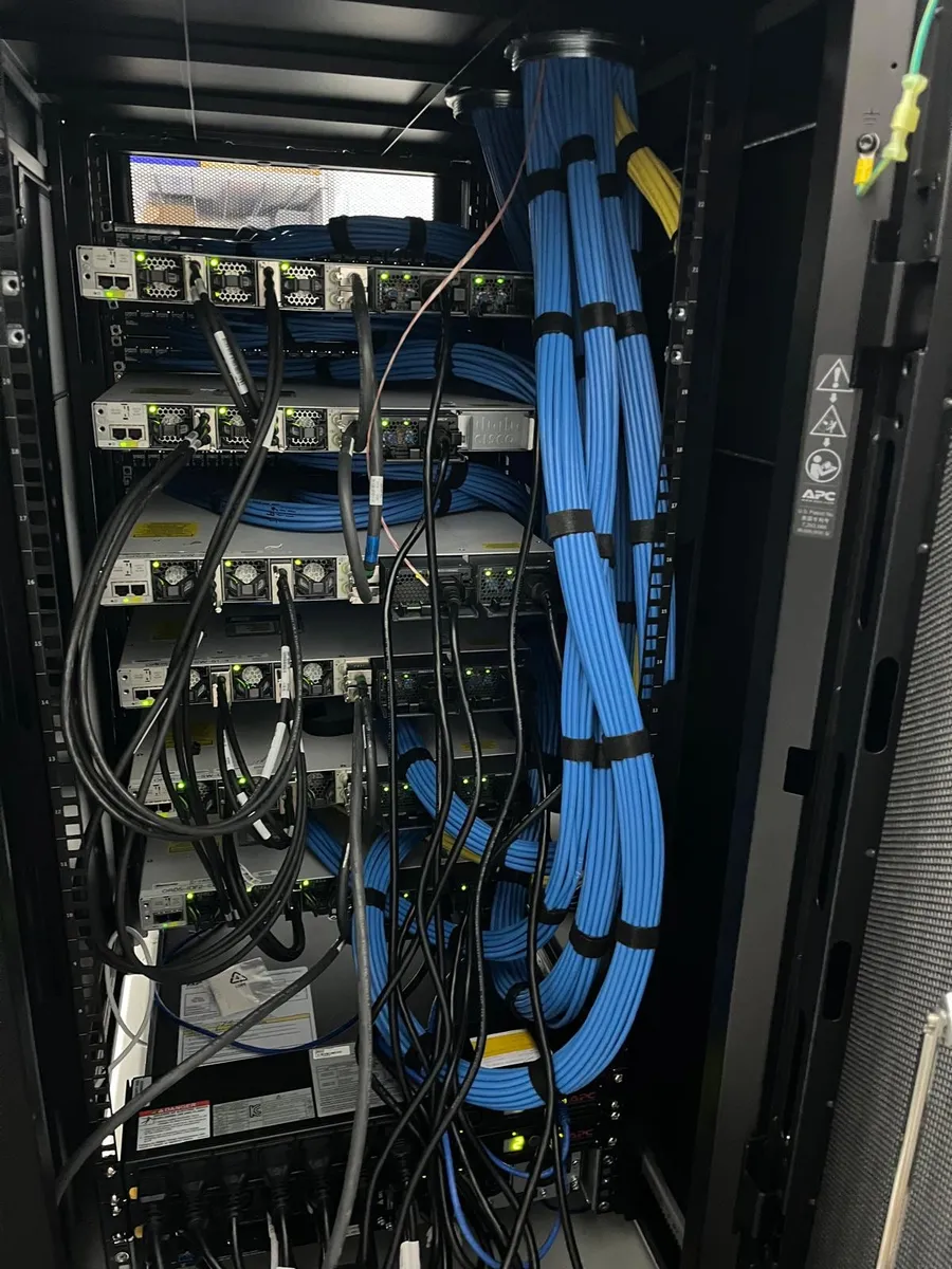 Finished network cabinet with stacked switches, dressed blue cable bundles and a UPS at the bottom