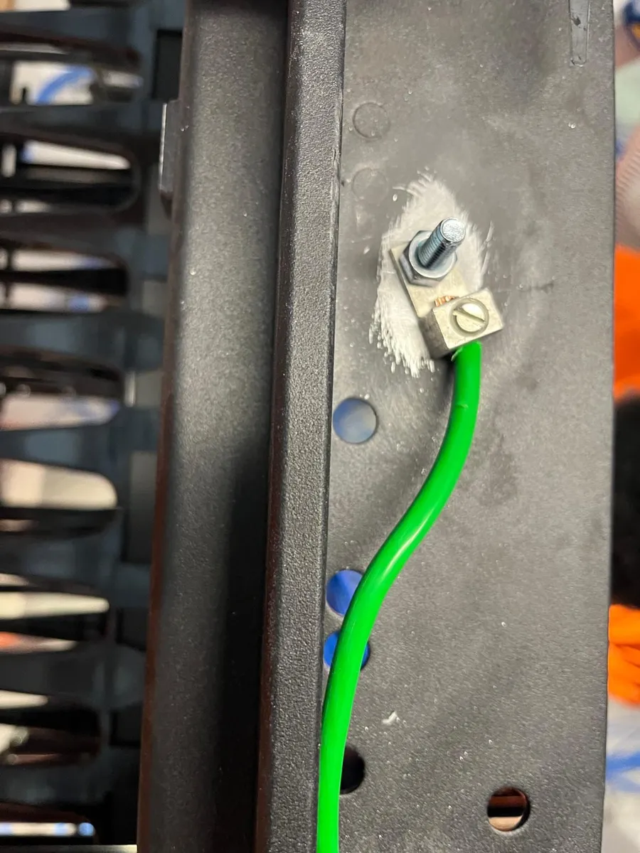 Close-up of a grounding lug and green ground wire bolted to a network rack