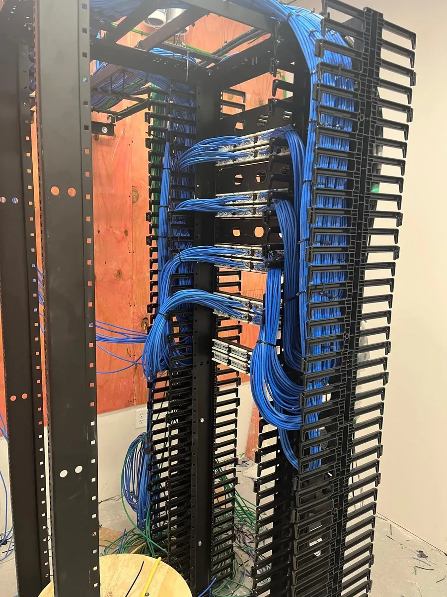 Two-post network rack with blue copper cable bundles being dressed into vertical cable managers